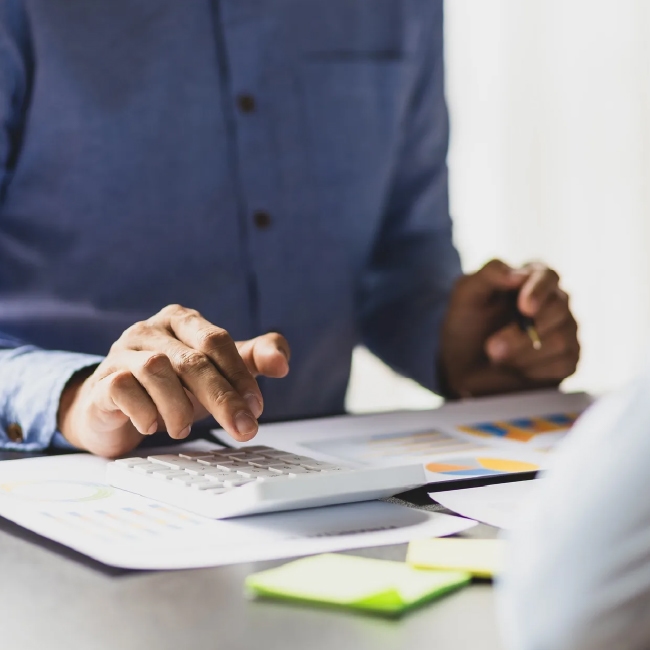 Person calculating finances with reports and calculator.