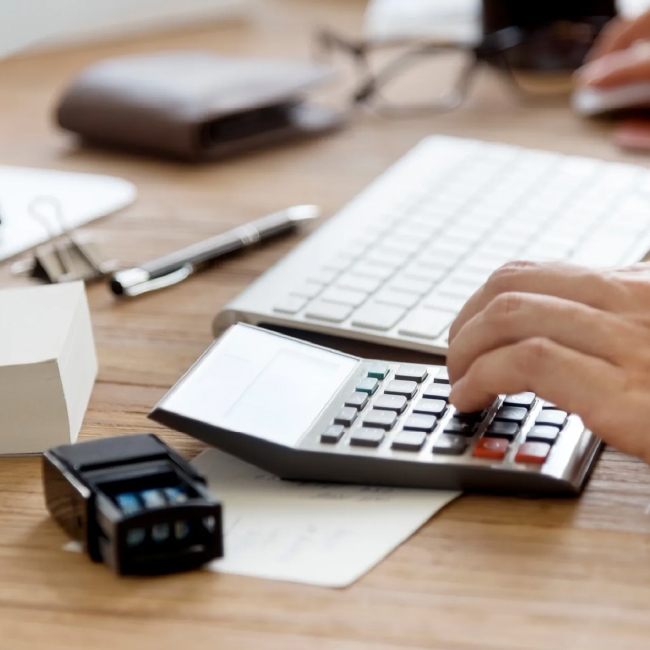 Person using calculator at desk with computer.